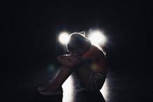 Lonely Child Sitting In Darkness Illuminated With Headlights On Black Background