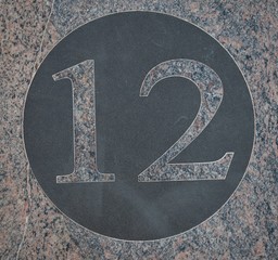 Number twelve black circle on pink marble.