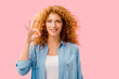 cheerful redhead girl showing ok sign isolated on pink