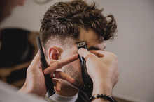 Young Man With Trendy Haircut At Barber Shop. Barber Does The Hairstyle And Beard Trim.