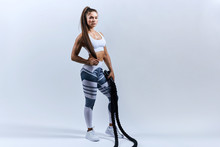 Sexy Tired Sportswoman After Battle Rope Workouts On White Background. Attractive Female Athlete Taking Rest After Fitness Training At Gym, Full Length Photo. Copy Space