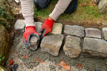 Wall Mural - pavement works, Cobbled pavement natural stone. gloved Hands of worker installing concrete paver blocks. Hands of a bricklayer laying paving stones carefully placing