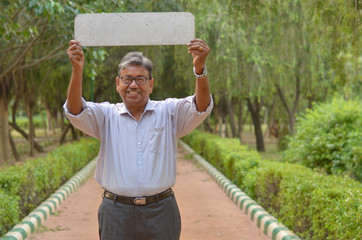 senior bengali indian man holding a blank placard which can be used for quotes above his head in a p