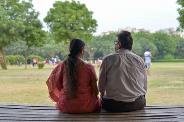 Wall Mural - Senior citizen couple shot from back relaxing, talking, sitting in a park in Delhi, India. Concept love