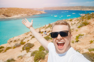 Wall Mural - Male tourist sunglasses taking selfie photo on beach Blue Lagoon Comino Malta