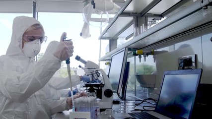 Wall Mural - scientists in protection suits and masks working in research lab using laboratory equipment: microsc