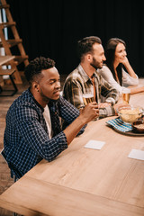 young multicultural friends drinking beer together in pub