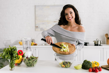 cheerful girl holding knife and cutting board near salad in bowl