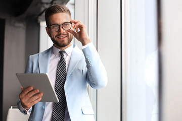 Wall Mural - Modern business man in formalwear using digital tablet while standing near window in the office