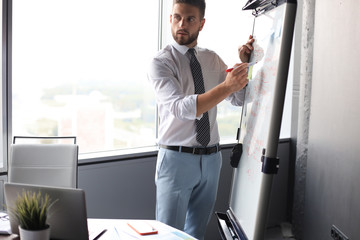 Wall Mural - Smart concentrated businessman writing something on the flipchart using marker