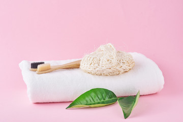 Two wooden bamboo eco friendly toothbrushes, towel and washcloth on a pink background