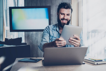 Smiling manager working effectively using digital tools. Programmer developing app for PC and tablet. Bearded hipster at workplace taking selfie on wireless device camera, shooting stories for blog.