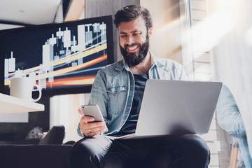 Male professional working on laptop and smartphone in office. Digital developer testing apps and synchronizing corporate programs. Manager taking selfie at workplace and posting images in social media