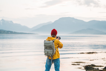 Traveler photographer wearing yellow raincoat taking photo by professional camera of fantastic scandinavia nature. Man tourist tourist travels to beautiful mountain and fjord places