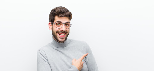 young manager man looking excited and surprised pointing to the side and upwards to copy space against white wall