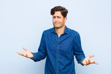 Wall Mural - young handsome man looking puzzled, confused and stressed, wondering between different options, feeling uncertain against blue background