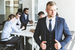 © xartproduction - Business man stands on the background of partners. A team of young businessmen working and communicating together in an office. Corporate businessteam and manager in a meeting.