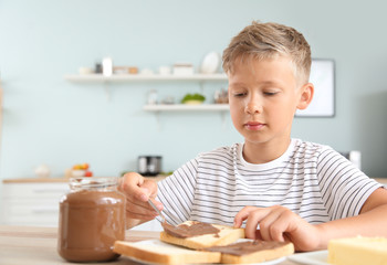 Canvas Print - Funny little boy eating tasty toasts with chocolate spreading in kitchen