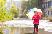 Little Girl In Rubber Boots Running Through A Puddle On A Rainy Day