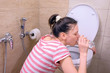 © familylifestyle - Pregnant young tired woman is vomiting in toilet sitting on the floor at home and drinking water, back view.