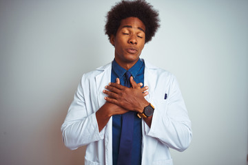 Wall Mural - Young african american doctor man wearing coat standing over isolated white background smiling with hands on chest with closed eyes and grateful gesture on face. Health concept.