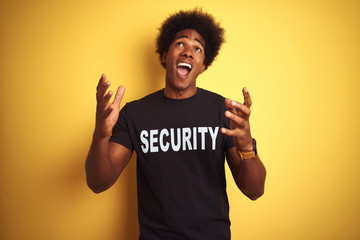 Poster - American safeguard man with afro hair wearing security uniform over isolated yellow background crazy and mad shouting and yelling with aggressive expression and arms raised. Frustration concept.