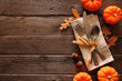 © Jenifoto - Autumn harvest or thanksgiving table scene with silverware, napkin, leaves and pumpkin border against a rustic dark wood background