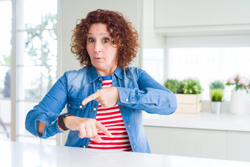 Wall Mural - Middle age senior woman with curly hair wearing denim jacket at home In hurry pointing to watch time, impatience, upset and angry for deadline delay