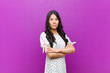 © kues1 - young pretty latin woman smiling to camera with crossed arms and a happy, confident, satisfied expression, lateral view against purple wall