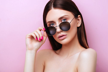 Wall Mural - Portrait of an attractive young girl in round glasses on a pink background in studio