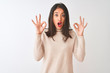 © Krakenimages.com - Beautiful chinese woman wearing turtleneck sweater standing over isolated white background looking surprised and shocked doing ok approval symbol with fingers. Crazy expression