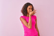 Young brazilian woman wearing t-shirt standing over isolated pink background smelling something stinky and disgusting, intolerable smell, holding breath with fingers on nose. Bad smells concept.