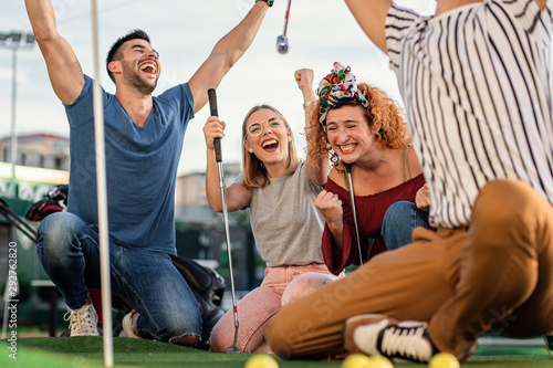Fotomural Group of smiling friends enjoying together playing mini golf in the city