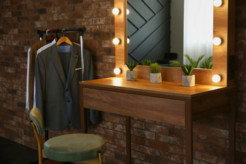 Table with mirror and male clothes in modern dressing room