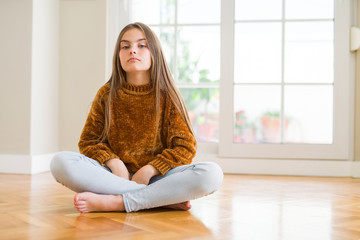 Wall Mural - Beautiful young girl kid sitting on the floor at home with serious expression on face. Simple and natural looking at the camera.