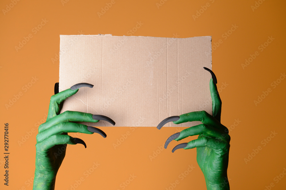 Hands of witch holding blank paper sheet on color background. Halloween celebration