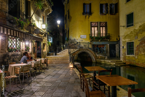 Narrow canal with bridge and tables of restaurant in Venice, Italy. Architect...