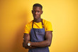 © Krakenimages.com - African american bartender man wearing apron standing over isolated yellow background skeptic and nervous, disapproving expression on face with crossed arms. Negative person.