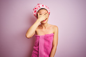 Sticker - Young beautiful woman wearing towel and bath hat after shower over pink isolated background smiling and laughing with hand on face covering eyes for surprise. Blind concept.