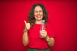 © Krakenimages.com - Middle age senior woman holding plastic water bottle over red isolated background happy with big smile doing ok sign, thumb up with fingers, excellent sign
