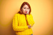 © Krakenimages.com - Beautiful redhead woman wearing winter sweater standing over isolated yellow background thinking looking tired and bored with depression problems with crossed arms.