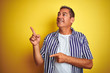 © Krakenimages.com - Handsome middle age man wearing striped shirt standing over isolated yellow background smiling and looking at the camera pointing with two hands and fingers to the side.