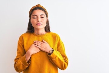 Wall Mural - Young beautiful woman wearing yellow sweater and diadem over isolated white background smiling with hands on chest with closed eyes and grateful gesture on face. Health concept.