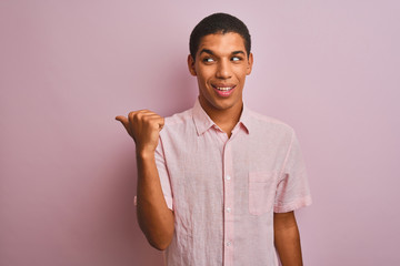 Young handsome arab man wearing casual shirt standing over isolated pink background smiling with happy face looking and pointing to the side with thumb up.