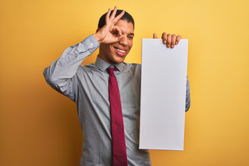 Young handsome arab businessman holding banner standing over isolated yellow background with happy face smiling doing ok sign with hand on eye looking through fingers