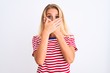 © Krakenimages.com - Young beautiful woman wearing red striped t-shirt standing over isolated white background shocked covering mouth with hands for mistake. Secret concept.