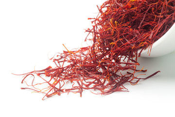 Dried saffron dumped from a white ceramic cup. Isolated on white background.