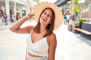 Young beautiful woman inside of shopping center, standing smiling happy and cheerful at the mall on a sunny day of summer