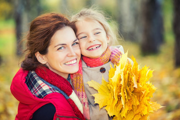 Smiling little girl and her mother enjoy walk in autumn park and play with bright autumn leaves