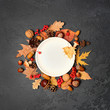 mpty white plate and autumn leaves, pumpkins, cones, acorns, berries on dark table. Autumn harvest season, Halloween and thanksgiving day table setting. Fall time. Thanksgiving background mock up.